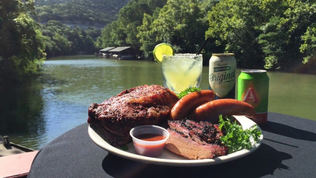 A plate of ribs and other barbeque food with a river in the background.