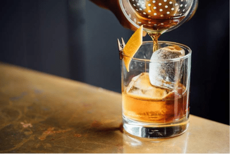 A glass of whiskey strained over ice in a tumbler.